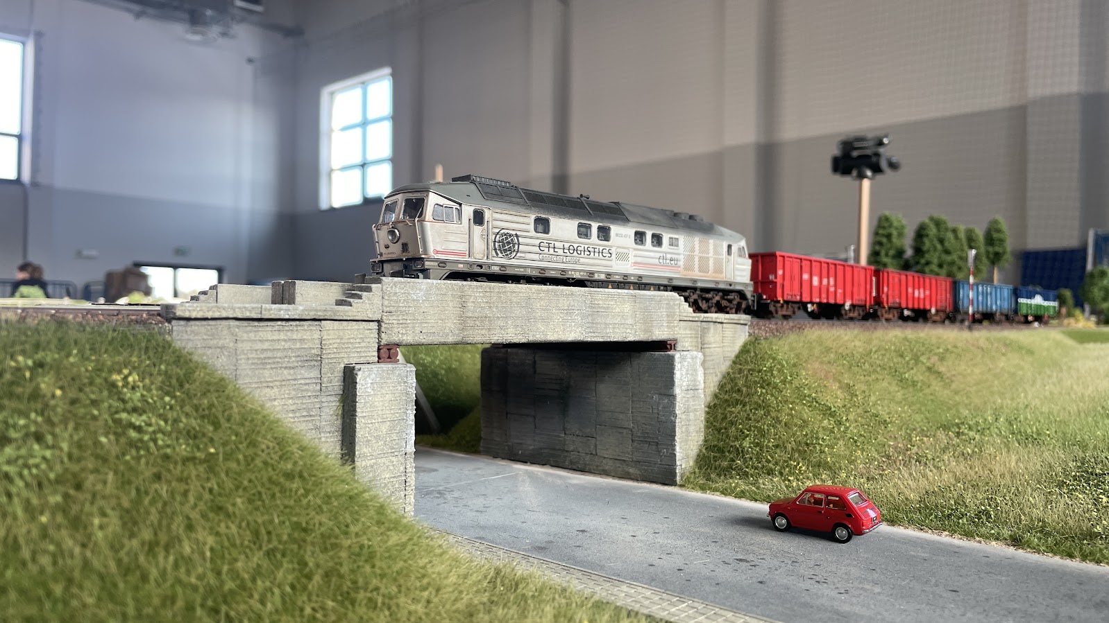 Model białej lokomotywy CTL z czerwonymi wagonami na moście i Fiatem 126p – BGM